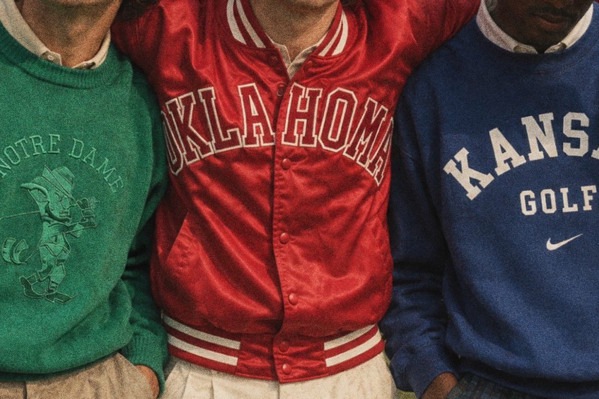 Three friends shoulder to shoulder in vintage college knits: a green Notre Dame sweater, a red satin Oklahoma jacket, and a blue Kansas Golf crewneck